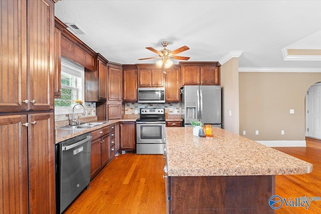 kitchen with appliances with stainless steel finishes, sink, hardwood / wood-style flooring, a center island, and light stone counters