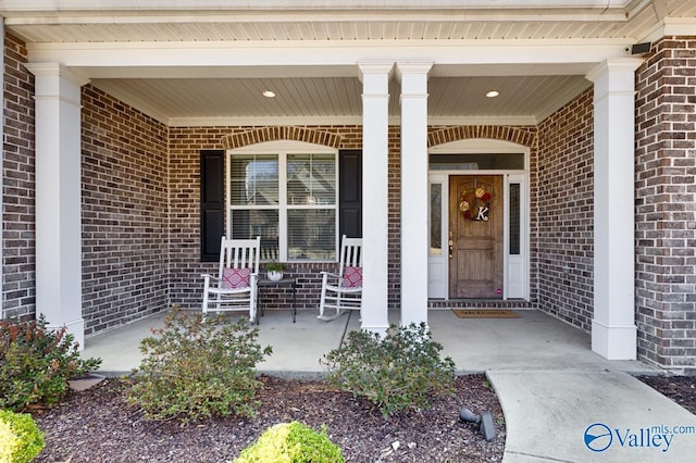 entrance to property featuring a porch and brick siding