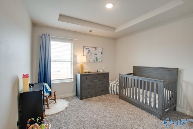 carpeted bedroom featuring a crib and a tray ceiling