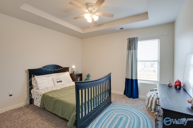 bedroom featuring a tray ceiling, light colored carpet, and ceiling fan