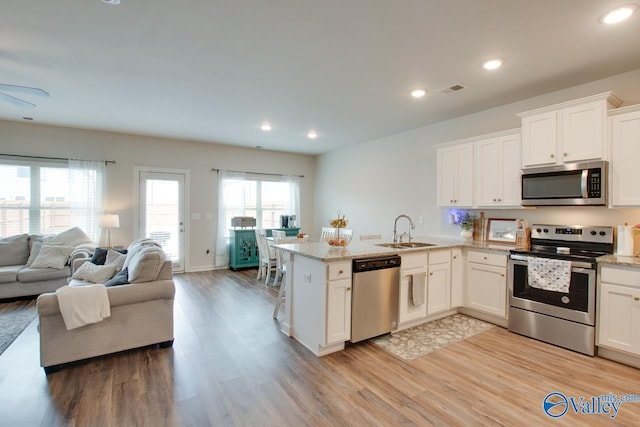 kitchen with appliances with stainless steel finishes, sink, white cabinets, light hardwood / wood-style floors, and light stone countertops