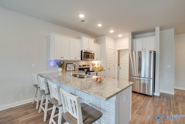 kitchen featuring sink, a breakfast bar area, white cabinets, light stone counters, and stainless steel appliances