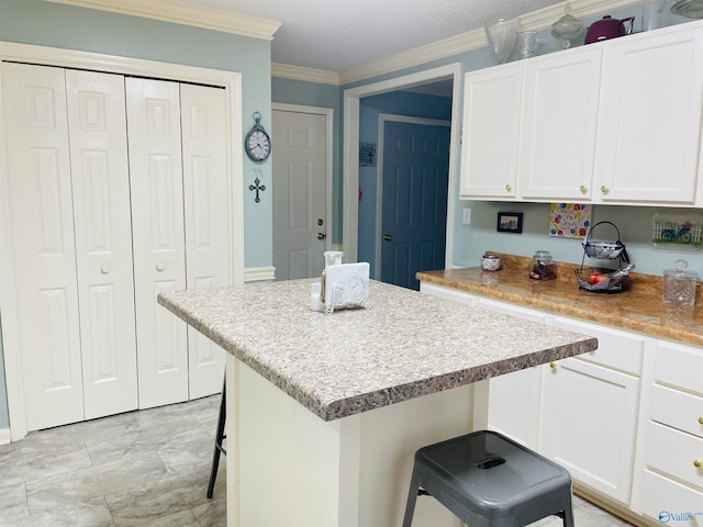 kitchen with ornamental molding, a kitchen bar, white cabinetry, and a center island