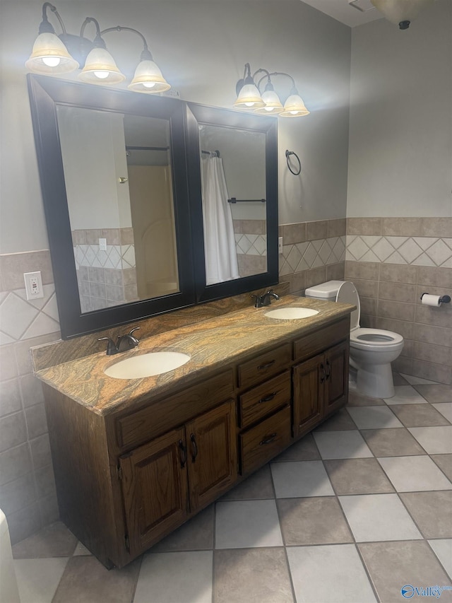 full bathroom with toilet, double vanity, a sink, and tile walls