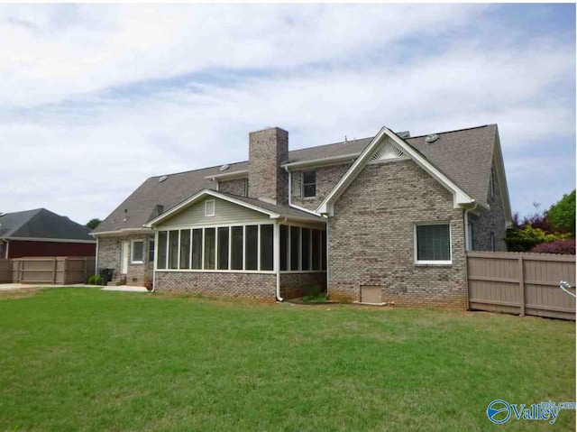 rear view of house with a fenced backyard, brick siding, a sunroom, a lawn, and a chimney