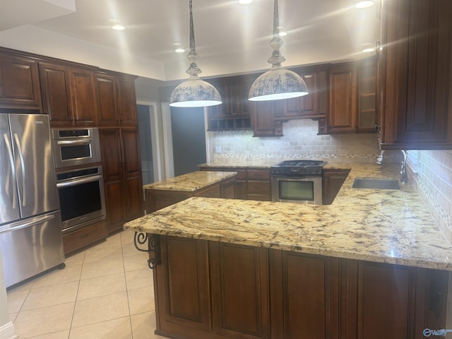 kitchen with pendant lighting, stainless steel appliances, a sink, dark brown cabinetry, and light stone countertops