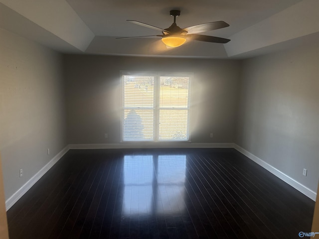 unfurnished room with a ceiling fan, a tray ceiling, dark wood-style flooring, and baseboards