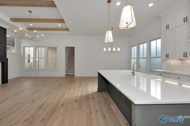 kitchen with hanging light fixtures, a sink, a large island with sink, and white cabinetry