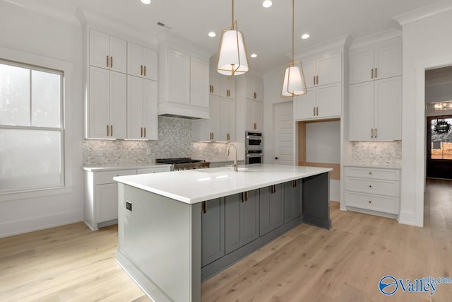 kitchen with an island with sink, white cabinets, light countertops, and pendant lighting