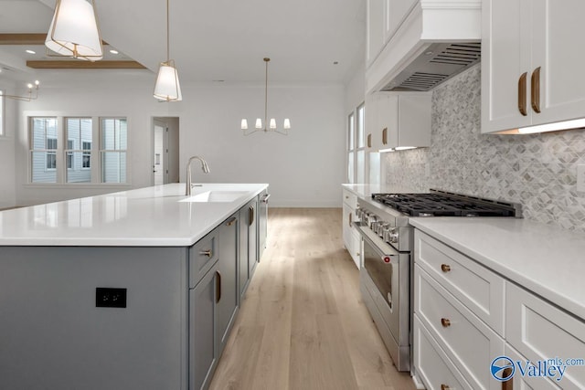 kitchen featuring stainless steel stove, light countertops, hanging light fixtures, an island with sink, and premium range hood