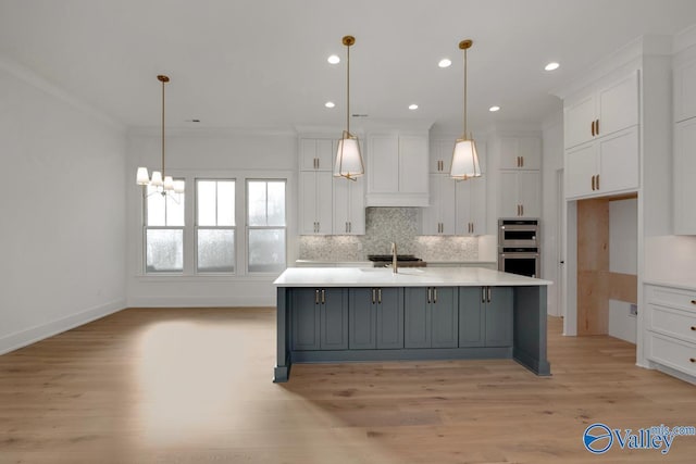 kitchen featuring white cabinets, pendant lighting, light countertops, and an island with sink