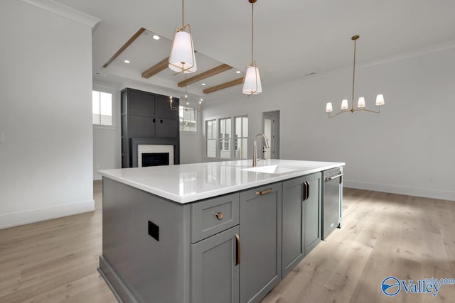 kitchen featuring gray cabinetry, a sink, light countertops, an island with sink, and decorative light fixtures