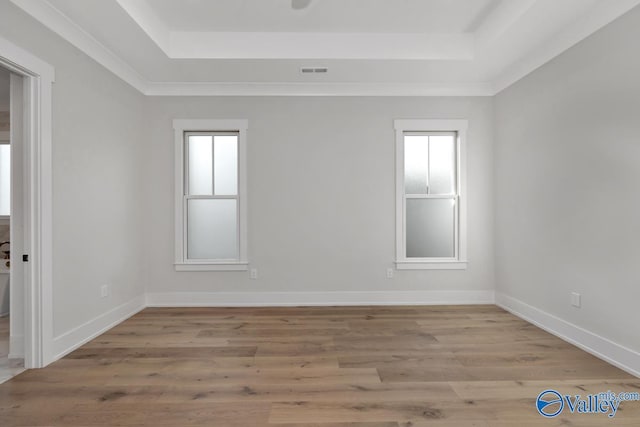 unfurnished room featuring light wood finished floors, a tray ceiling, visible vents, and baseboards