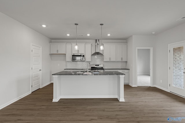 kitchen featuring a kitchen island with sink, dark stone counters, appliances with stainless steel finishes, dark hardwood / wood-style flooring, and white cabinetry