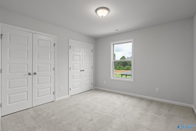 unfurnished bedroom with light carpet and two closets