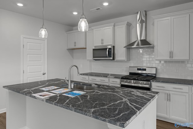 kitchen with a center island with sink, wall chimney exhaust hood, pendant lighting, and appliances with stainless steel finishes