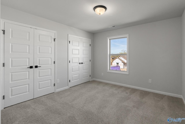 unfurnished bedroom with light colored carpet and multiple closets