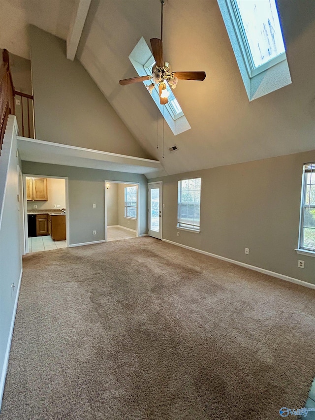 unfurnished living room with a skylight, light colored carpet, high vaulted ceiling, ceiling fan, and beam ceiling