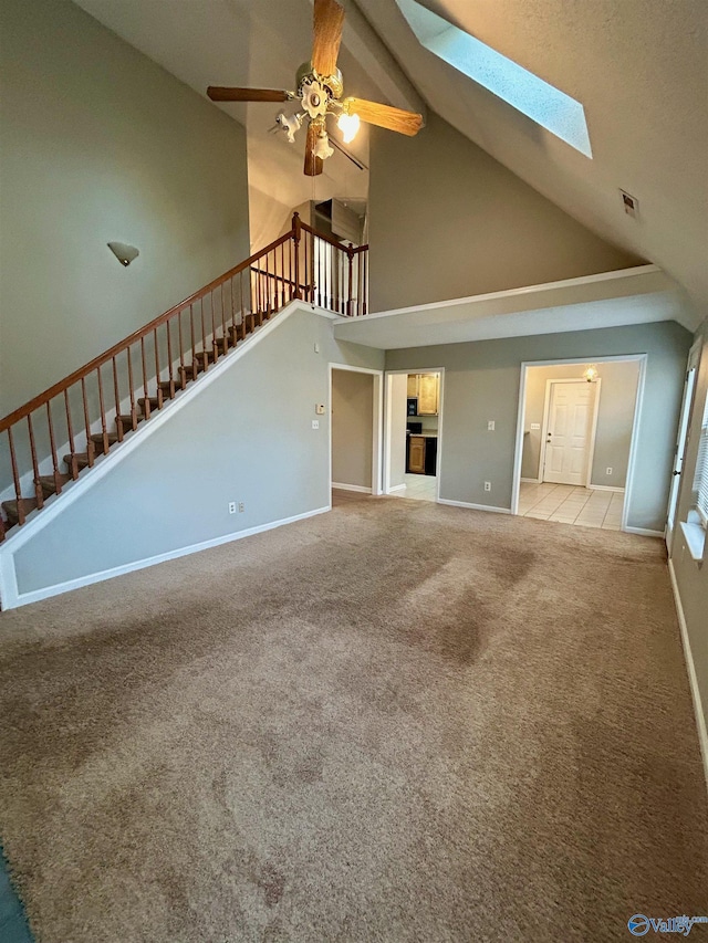 unfurnished living room with ceiling fan, light colored carpet, a skylight, and high vaulted ceiling