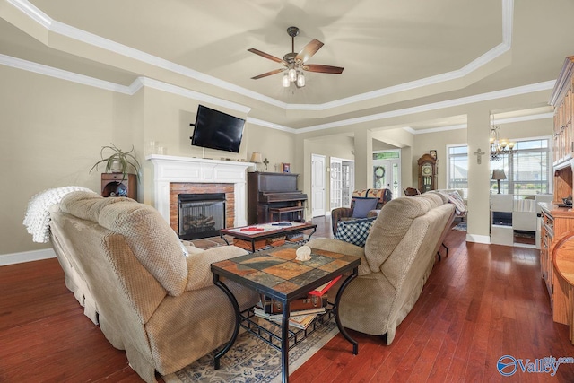 living room featuring dark hardwood / wood-style flooring, a tray ceiling, a fireplace, and crown molding