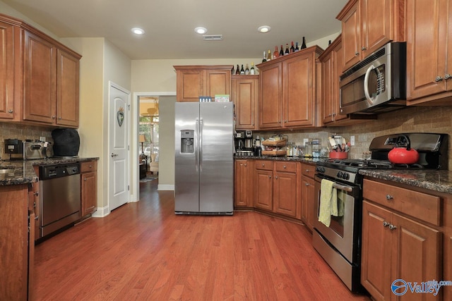 kitchen featuring stainless steel appliances, wood-type flooring, dark stone countertops, and decorative backsplash