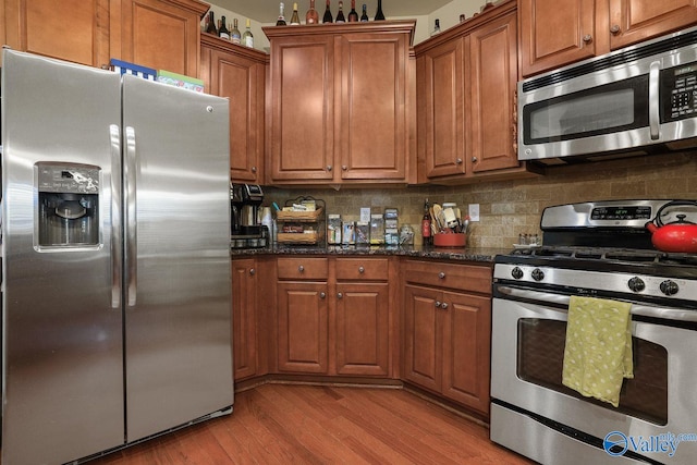 kitchen featuring tasteful backsplash, stainless steel appliances, light hardwood / wood-style floors, and dark stone countertops