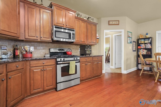 kitchen featuring backsplash, stainless steel appliances, dark stone counters, and light wood-type flooring