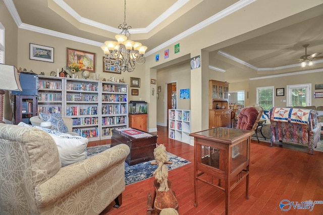 living area featuring a tray ceiling, wood-type flooring, ornamental molding, and ceiling fan with notable chandelier