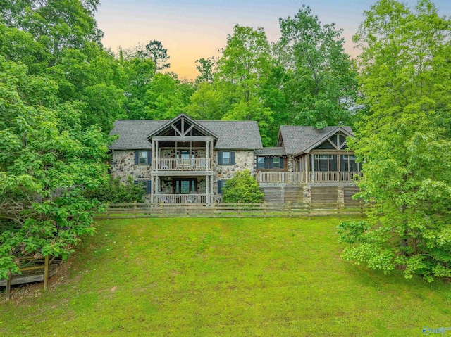chalet / cabin with stone siding, a balcony, and a front yard