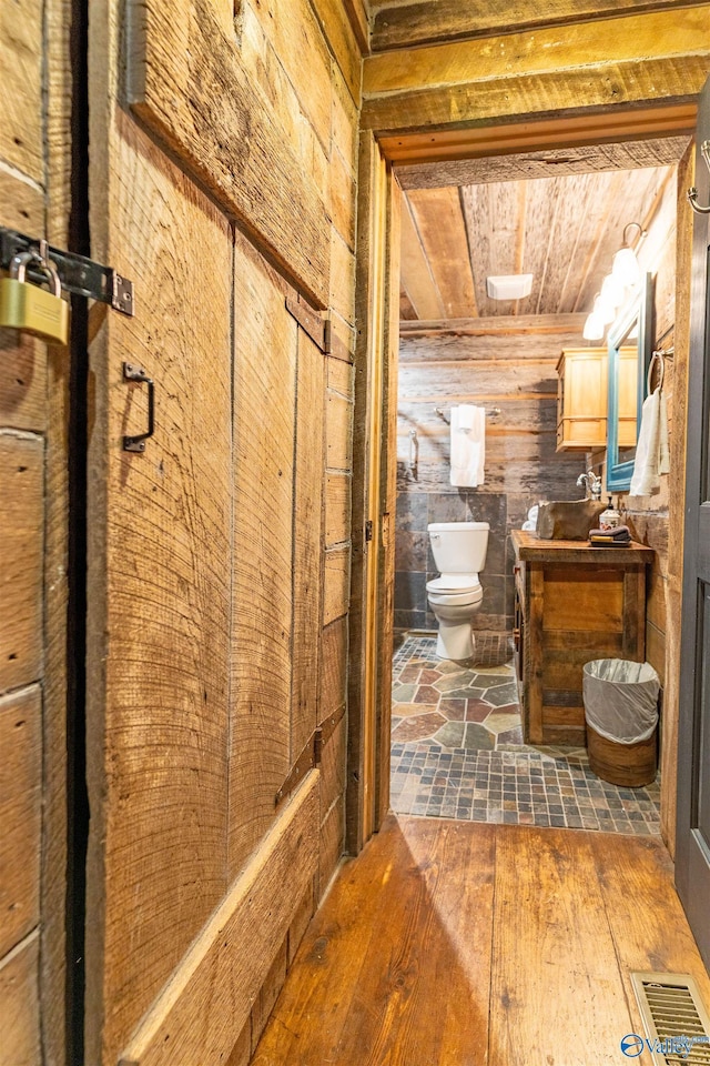 bathroom featuring visible vents, hardwood / wood-style flooring, wood walls, vanity, and toilet