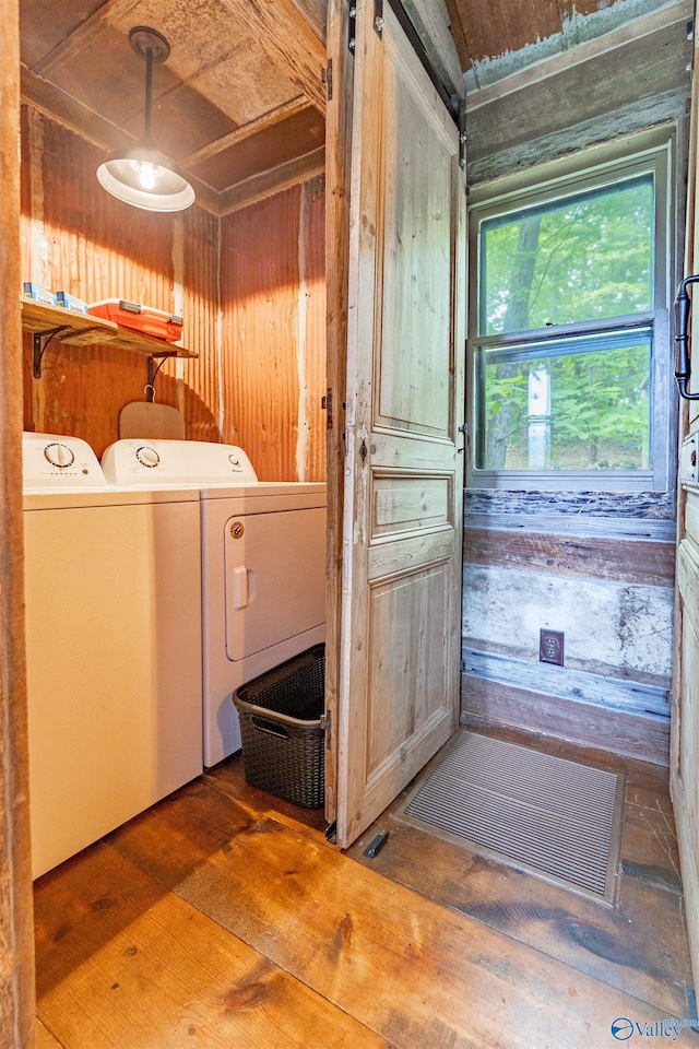 clothes washing area featuring wooden walls, laundry area, wood finished floors, and washer and clothes dryer