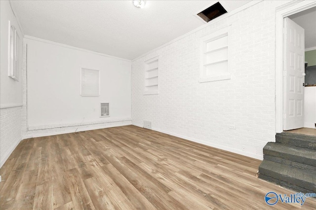 unfurnished room featuring hardwood / wood-style floors, built in features, ornamental molding, and brick wall