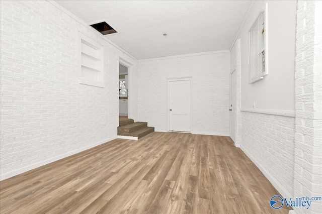 interior space with crown molding, brick wall, a textured ceiling, and wood-type flooring