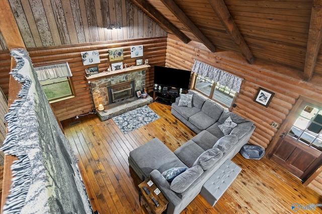 living room featuring hardwood / wood-style flooring, wooden ceiling, a stone fireplace, and vaulted ceiling with beams