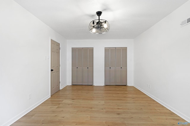 unfurnished bedroom with light hardwood / wood-style floors, two closets, and a chandelier