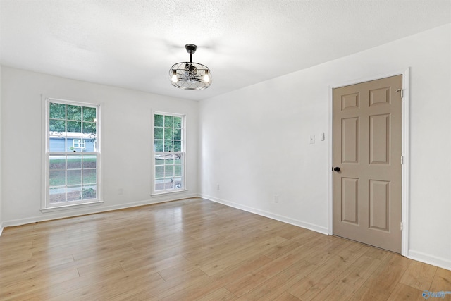 unfurnished room featuring a notable chandelier, light hardwood / wood-style floors, and a textured ceiling