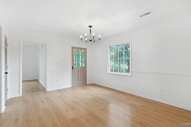 unfurnished room featuring a notable chandelier, light wood-type flooring, ornamental molding, and a textured ceiling