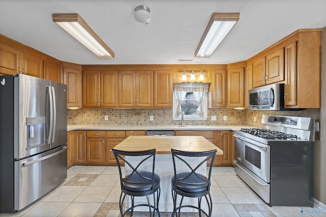 kitchen with light tile patterned flooring, a kitchen bar, appliances with stainless steel finishes, a kitchen island, and backsplash