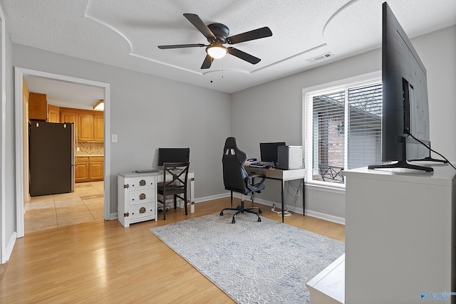 office space featuring ceiling fan, light hardwood / wood-style flooring, and a textured ceiling