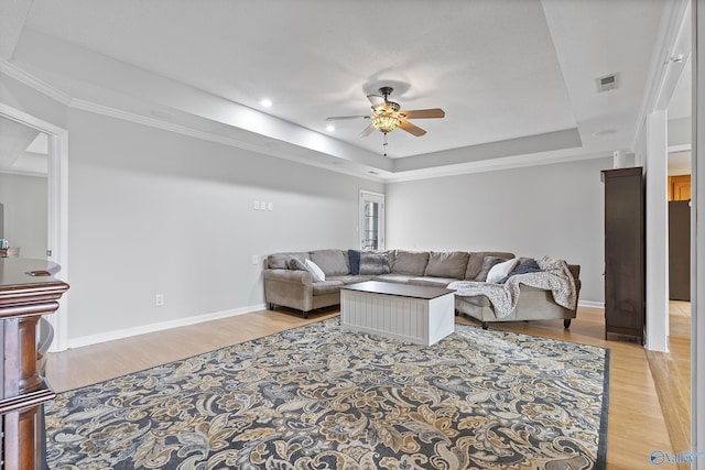 living room with crown molding, light hardwood / wood-style floors, a raised ceiling, and ceiling fan