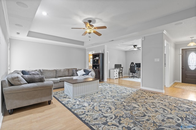 living room with crown molding, light hardwood / wood-style flooring, a raised ceiling, and ceiling fan