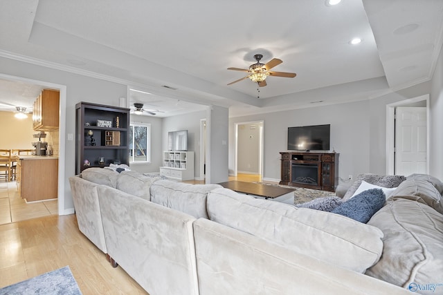 living room with a raised ceiling, ceiling fan, and light wood-type flooring