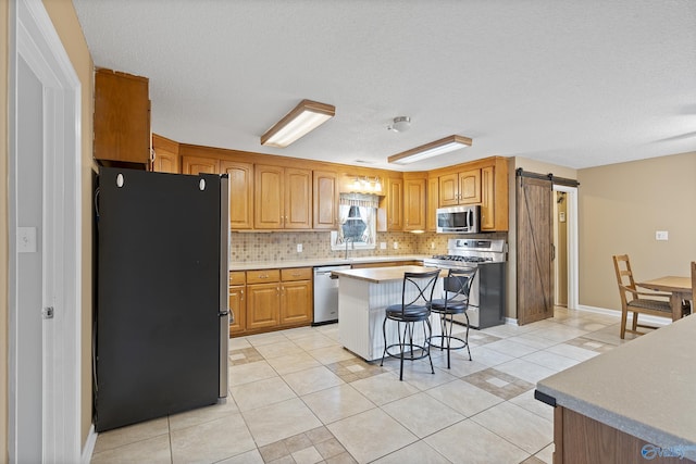 kitchen with appliances with stainless steel finishes, backsplash, a kitchen bar, a center island, and a barn door