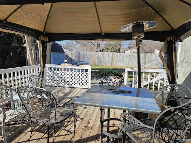 wooden terrace featuring fence, a shed, a gazebo, an outdoor structure, and outdoor dining space