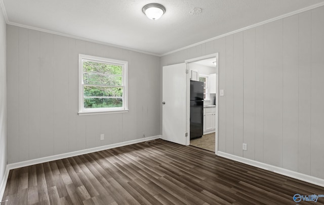 unfurnished bedroom with black refrigerator, dark hardwood / wood-style flooring, ornamental molding, and wooden walls