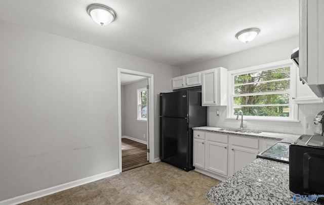 kitchen featuring black refrigerator, tasteful backsplash, light stone counters, sink, and white cabinetry