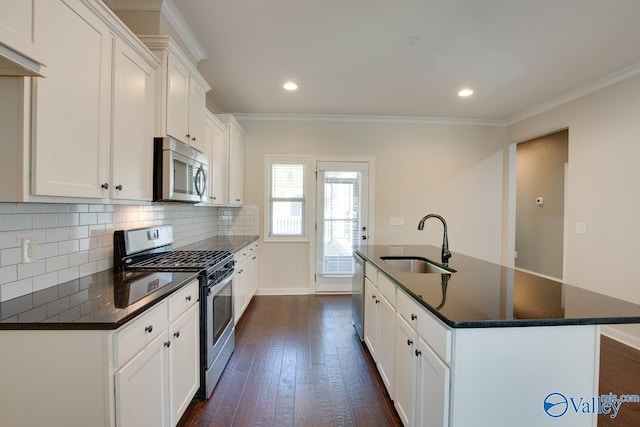 kitchen featuring an island with sink, stainless steel appliances, a sink, decorative backsplash, and dark wood-style flooring
