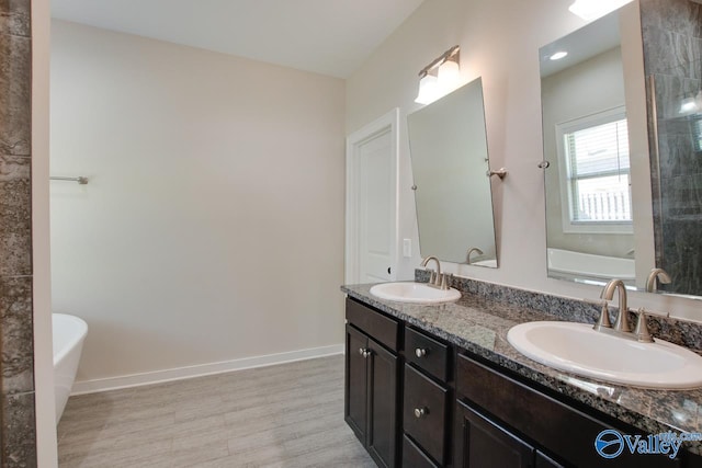 full bath with a freestanding tub, wood finished floors, a sink, and double vanity