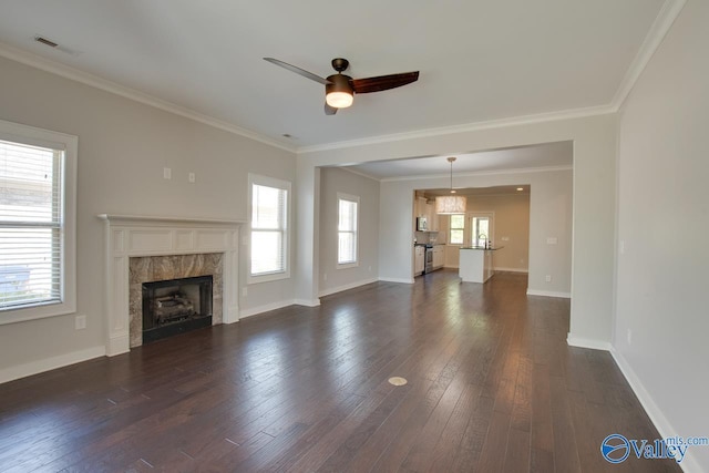 unfurnished living room with visible vents, a premium fireplace, ceiling fan, dark wood-type flooring, and ornamental molding