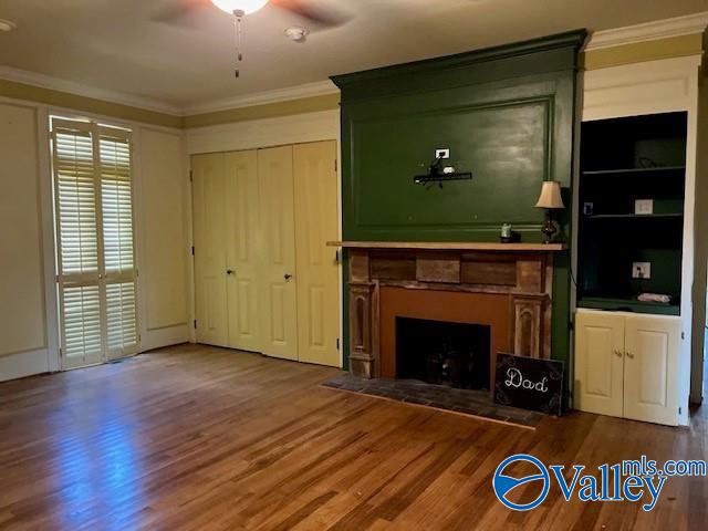 unfurnished living room with ornamental molding, built in shelves, ceiling fan, and hardwood / wood-style floors